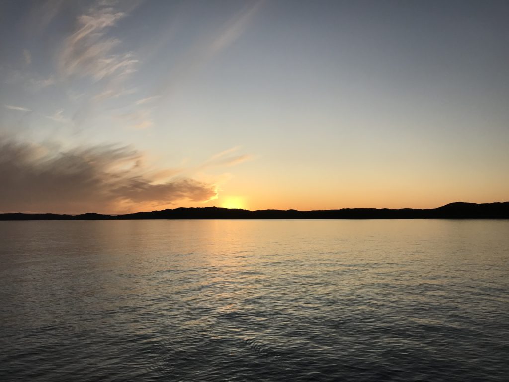 A thin island in silhouette against a sunset with the colours reflected in the sea. Solo travel means you can really focus on what you're experiencing.